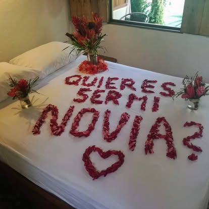 Rose petal heart decoration on a hotel bed with tropical flowers