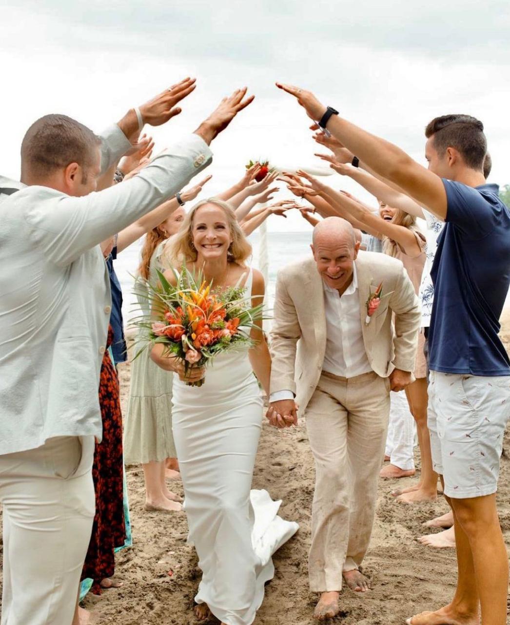 Bride walking through an arch of raised hands on the beach